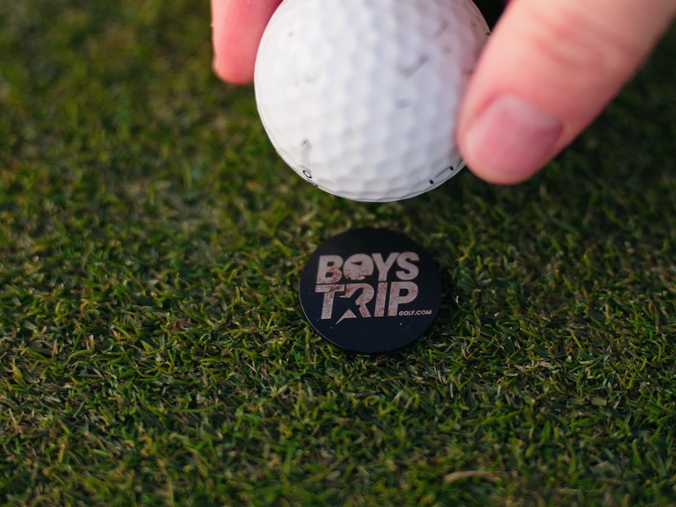 A Boys Trip Golf ball marker and ball teed up on the grass