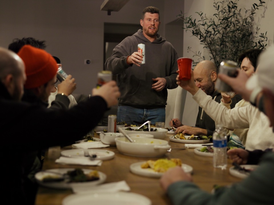 The crew raising a toast at a long dinner table in the house